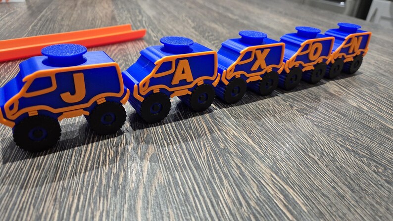 May include: A toy train made of blue and orange plastic with wheels. The train cars are connected and each car has a letter on it, spelling out the word "JAXON".