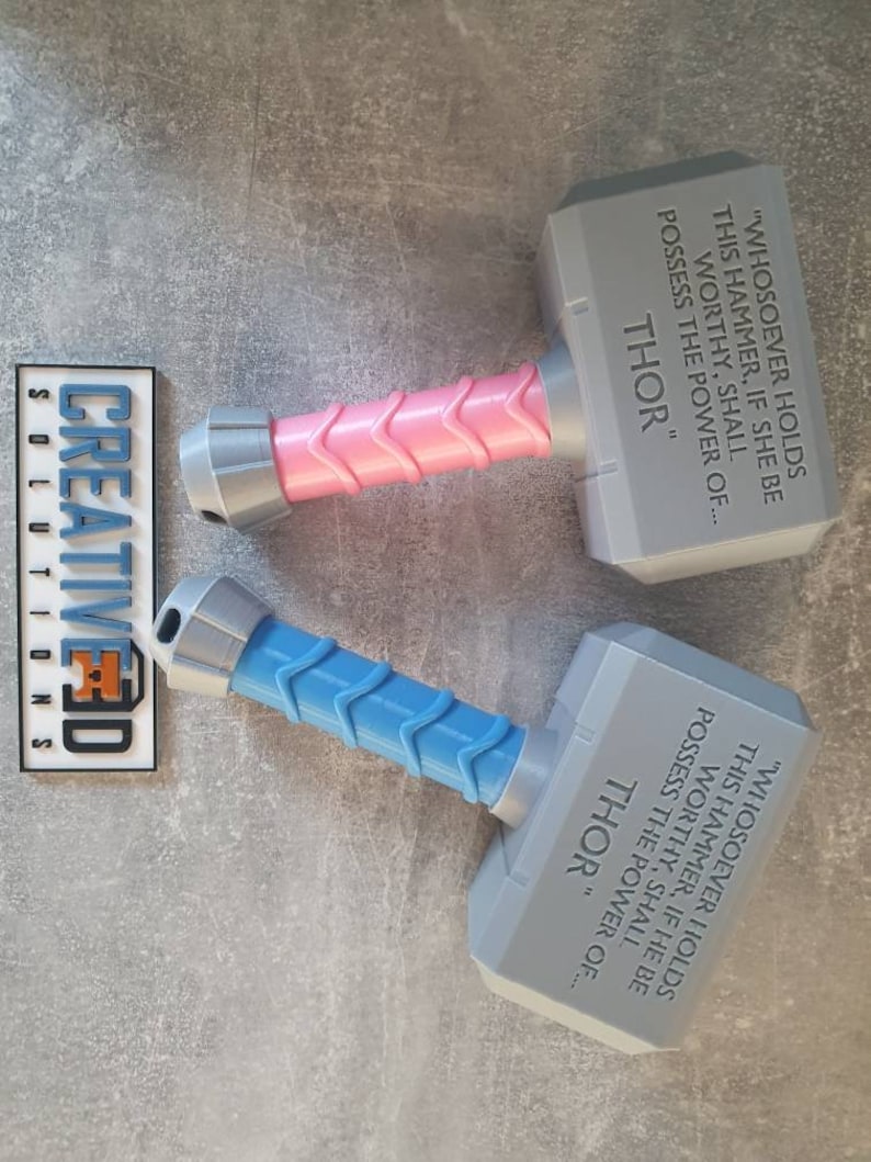 May include: Two gray plastic toy hammers with blue and pink handles. The hammers have the inscription "Whosoever holds this hammer, if she be worthy, shall possess the power of... Thor" on them.