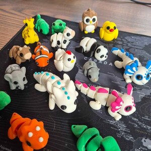 May include: A collection of colorful, small animal figurines, including a giraffe, owl, panda, and dragon. The figurines are made of a smooth material and are arranged on a black surface with a world map design.