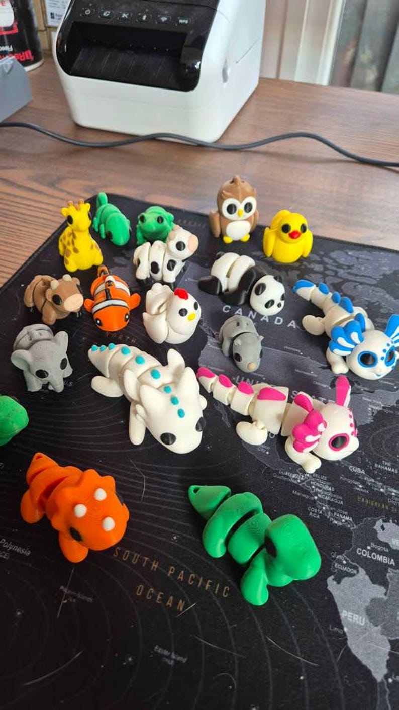 May include: A collection of colorful, small animal figurines, including a giraffe, owl, panda, and dragon. The figurines are made of a smooth material and are arranged on a black surface with a world map design.