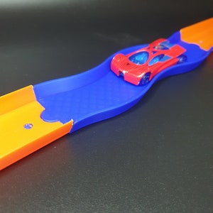 May include: A red toy car races down a blue and orange plastic track.
