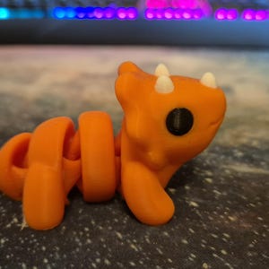May include: Orange and white segmented toy with a dinosaur-like head and large black eyes.