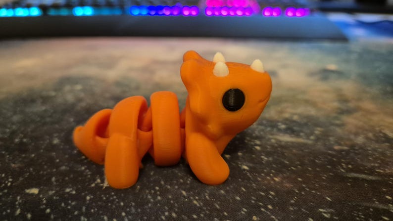 May include: Orange and white segmented toy with a dinosaur-like head and large black eyes.