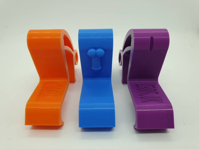 May include: Three 3D printed door stops in orange, blue, and purple. Each door stop has a different design. The orange door stop has the word "CAUTION" printed on it. The blue door stop has a small, raised, phallic symbol. The purple door stop has the words "Get a Life" printed on it.