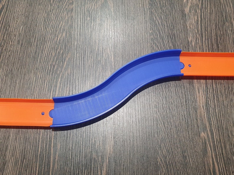 May include: A blue and orange plastic track piece for a toy car racing set. The track is curved and has two sections that connect together.
