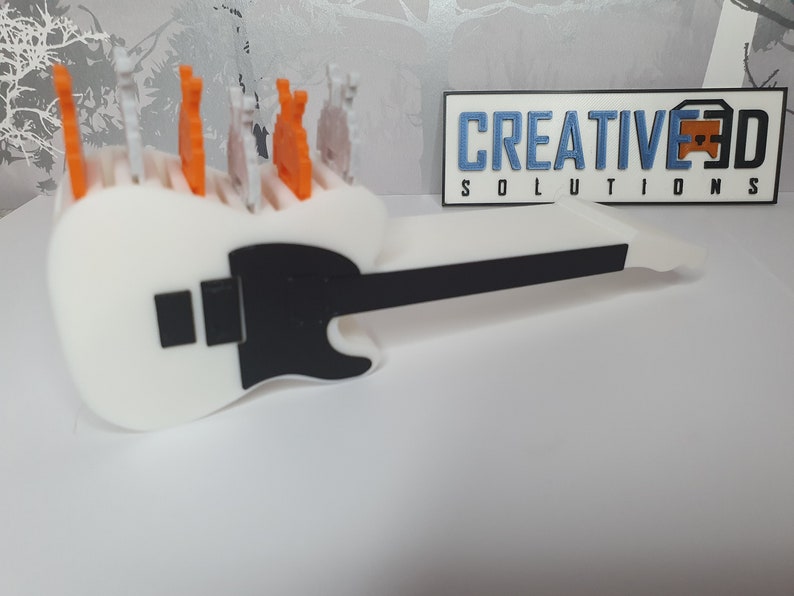 May include: White 3D printed guitar with a black pickguard and a black neck. The guitar has a row of small orange and white 3D printed figures on top.