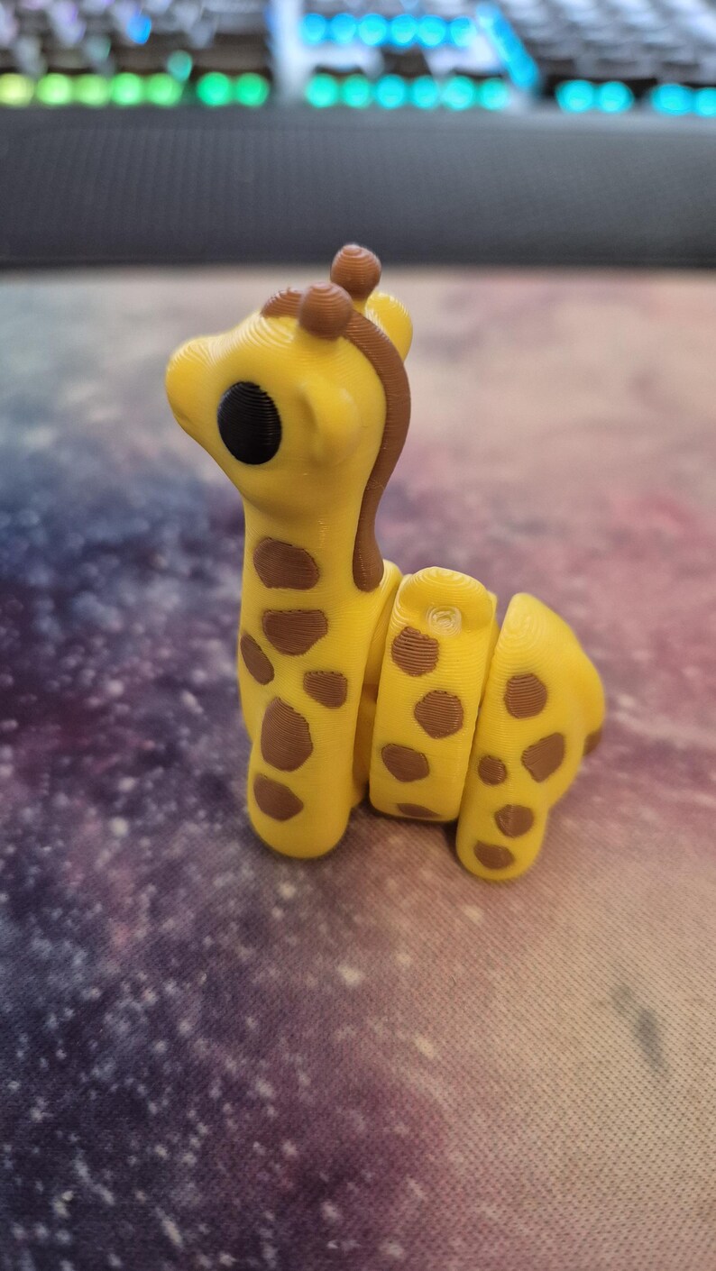May include: A yellow and brown giraffe figurine with a segmented body. The giraffe has a black eye and a brown nose.