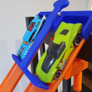 Op de afbeelding: Een blauwe en groene speelgoedauto racebaanset met twee speelgoedauto's, een blauwe en een groene, die de baan af racen.