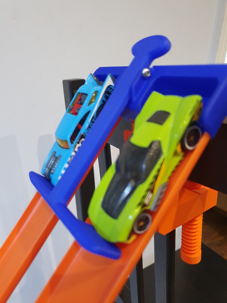 Op de afbeelding: Een blauwe en groene speelgoedauto racebaanset met twee speelgoedauto's, een blauwe en een groene, die de baan af racen.