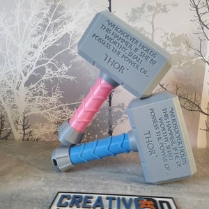 May include: Two gray plastic toy hammers with pink and blue handles. The hammers have the inscription "WHOSOEVER HOLDS THIS HAMMER, IF SHE BE WORTHY, SHALL POSSESS THE POWER OF... THOR" on them.