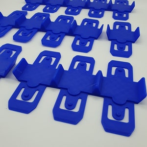 K&ouml;nnte beinhalten: Ein Satz von 15 blauen Wandhalterungen aus Kunststoff, die f&uuml;r die Befestigung von Gegenst&auml;nden wie Kabeln, Leitungen oder Dr&auml;hten konzipiert sind. Die Halterungen sind in Reihen angeordnet und aus strapazierf&auml;higem, flexiblem Kunststoff gefertigt.