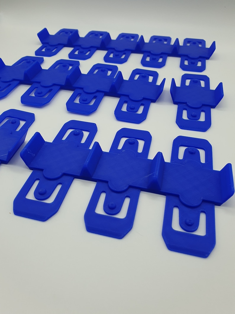 K&ouml;nnte beinhalten: Ein Satz von 15 blauen Wandhalterungen aus Kunststoff, die f&uuml;r die Befestigung von Gegenst&auml;nden wie Kabeln, Leitungen oder Dr&auml;hten konzipiert sind. Die Halterungen sind in Reihen angeordnet und aus strapazierf&auml;higem, flexiblem Kunststoff gefertigt.