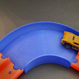 May include: A blue and orange plastic toy race track with a yellow toy car on the track.