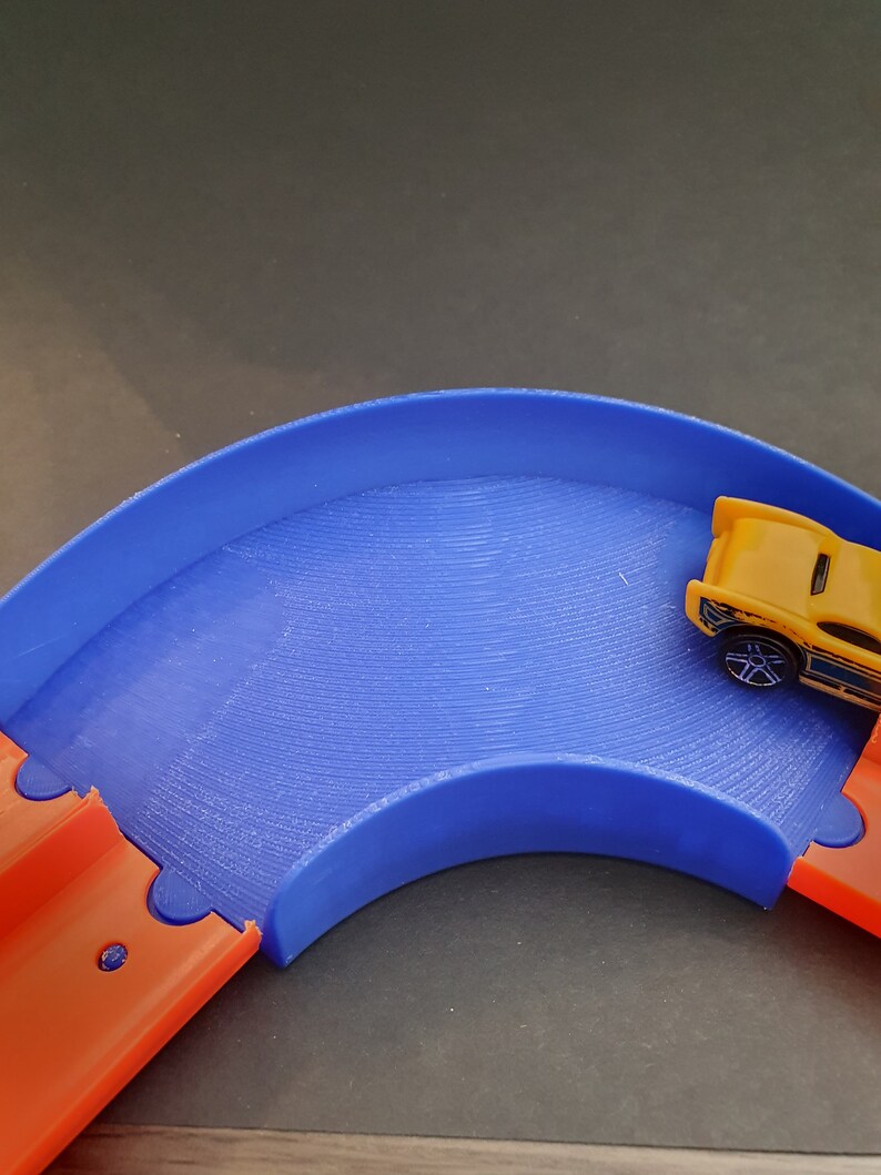 May include: A blue and orange plastic toy race track with a yellow toy car on the track.