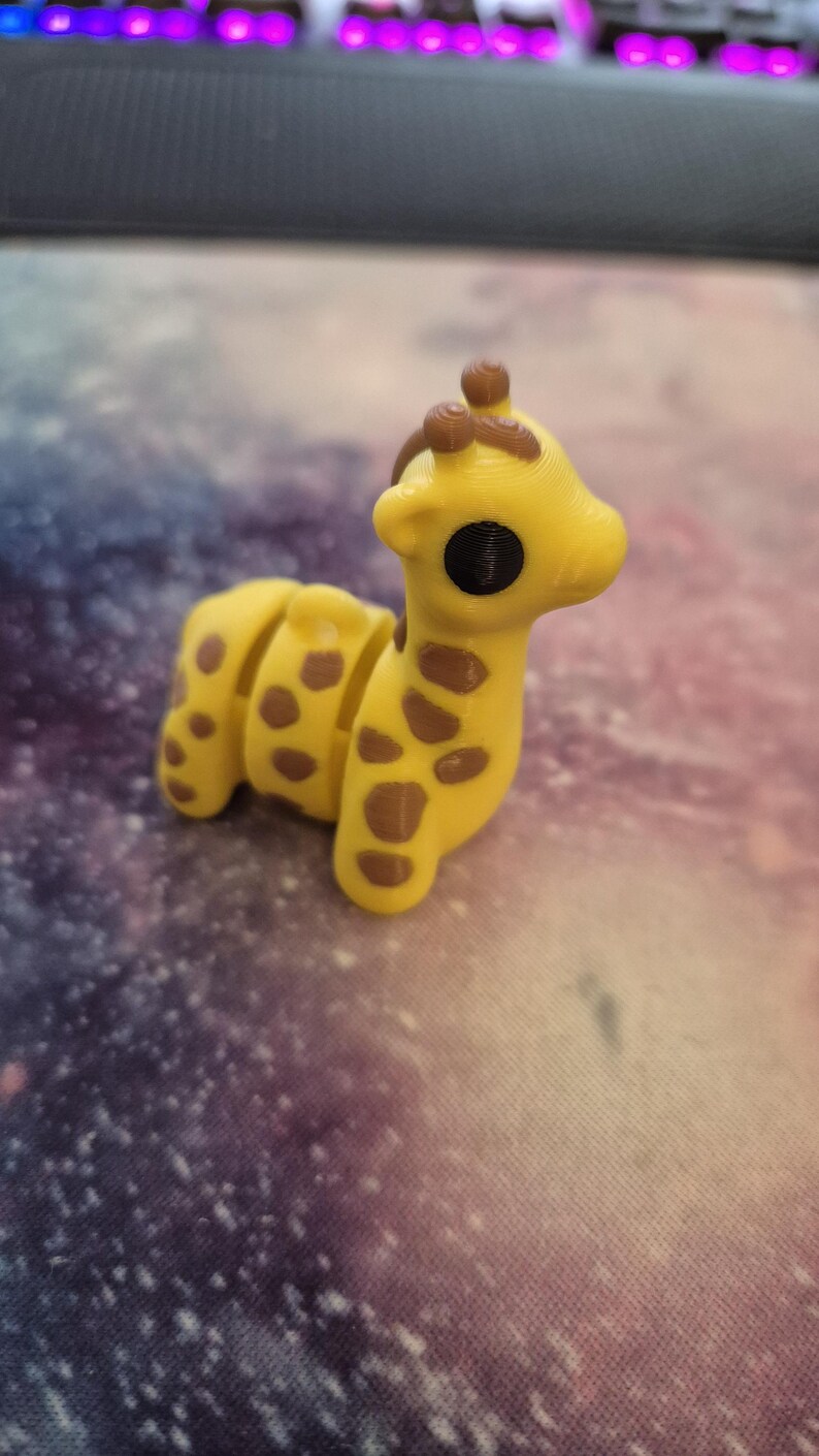 May include: A small yellow giraffe figurine with brown spots. The giraffe has a long neck and a small head with large black eyes.