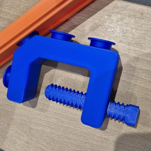 May include: A blue plastic clamp with a screw-like handle. The clamp has two blue rubber pads on the top.