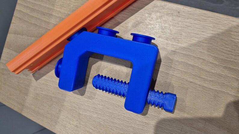 May include: A blue plastic clamp with a screw-like handle. The clamp has two blue rubber pads on the top.