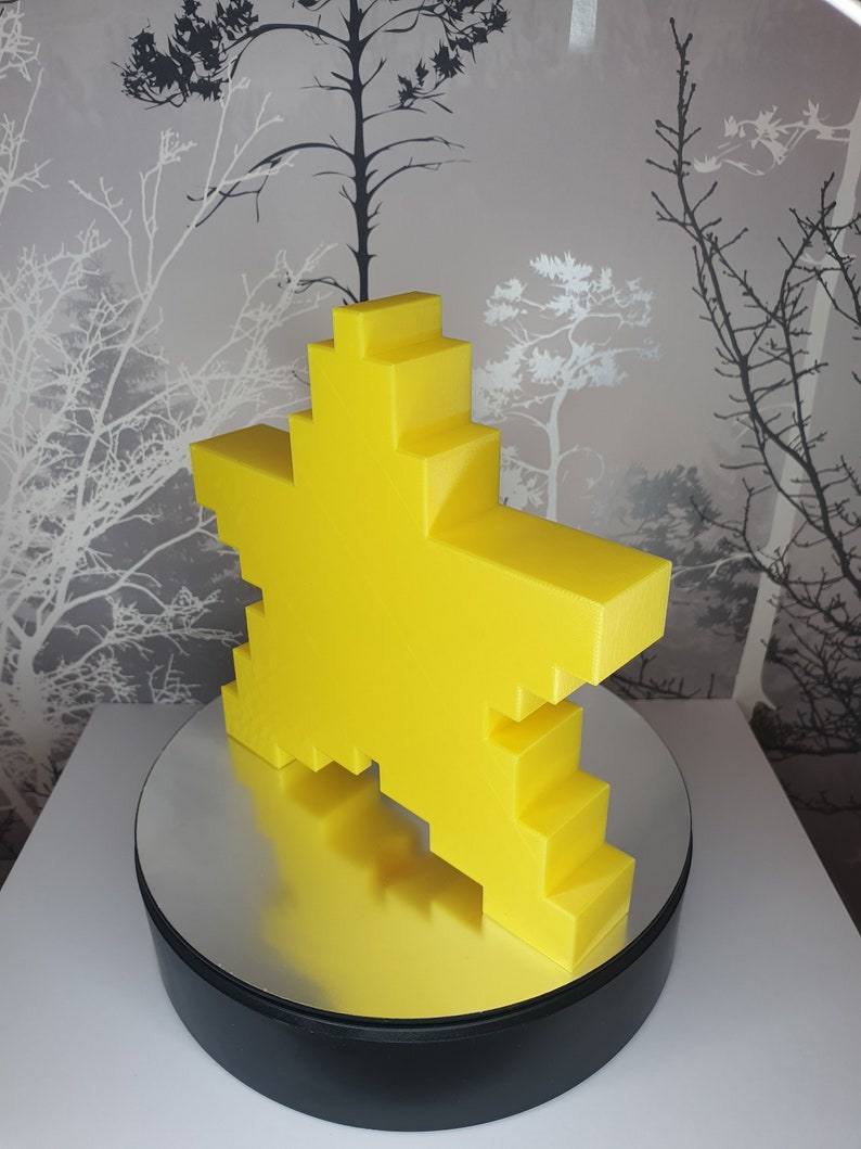 Puede incluir: Una escultura amarilla en forma de estrella pixelada sobre una base giratoria negra y plateada.