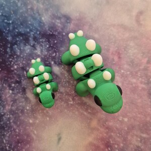 May include: Two green segmented toy dinosaurs with white spots. The larger dinosaur is about 5 inches long and the smaller dinosaur is about 3 inches long.
