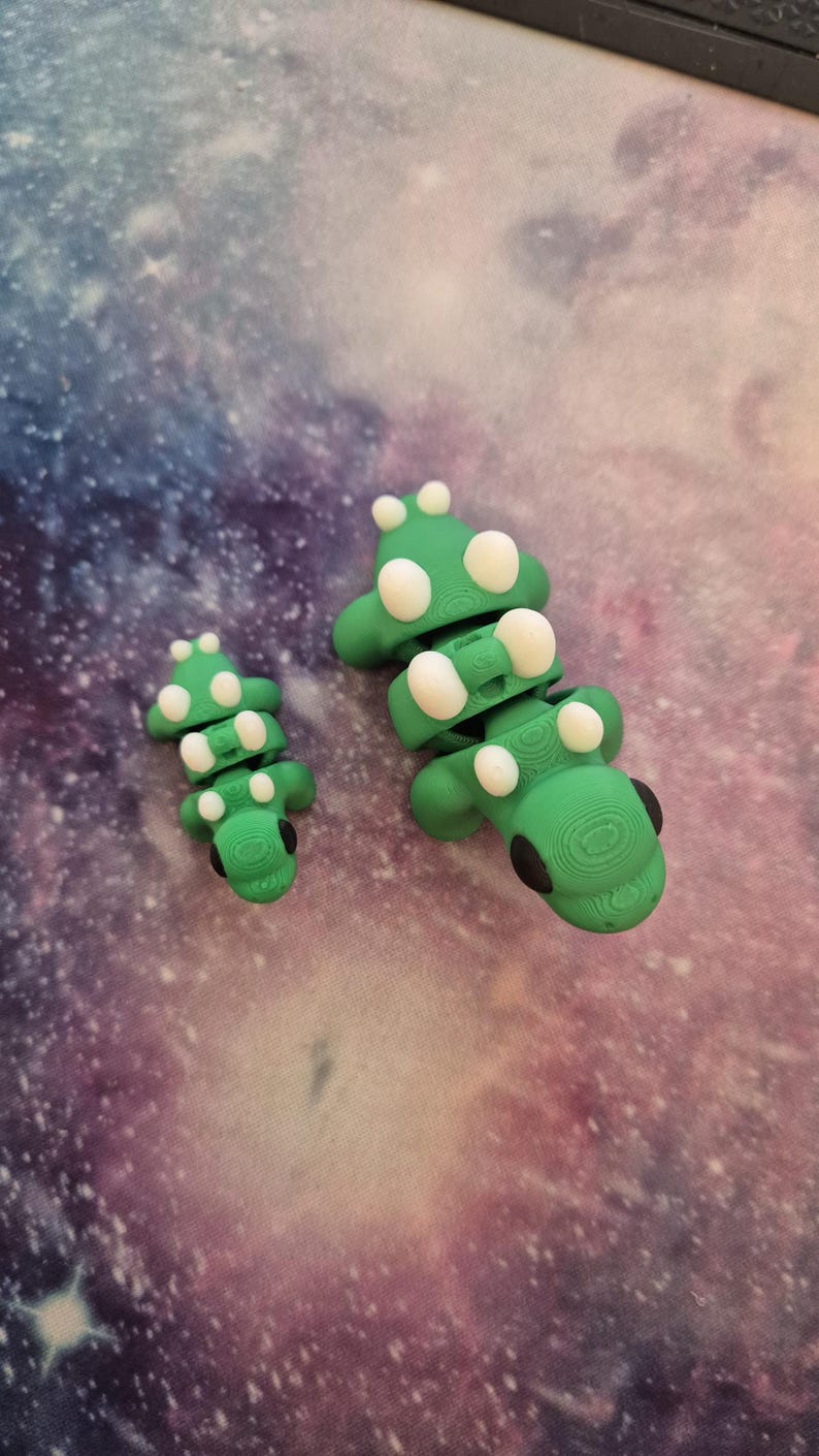 May include: Two green segmented toy dinosaurs with white spots. The larger dinosaur is about 5 inches long and the smaller dinosaur is about 3 inches long.