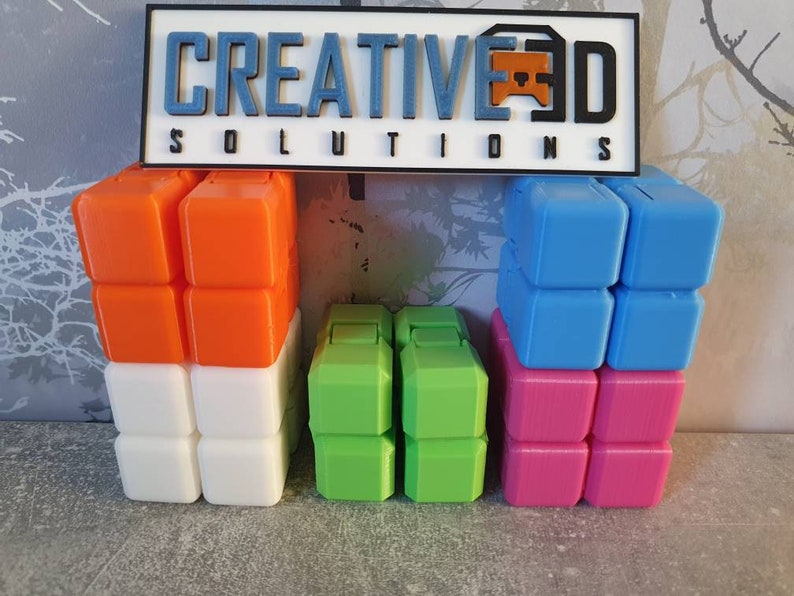 Op de afbeelding: Een set van vier 2x2 kubuspuzzels in oranje, wit, groen en roze. De kubussen zijn in een rij gestapeld, met de oranje en witte kubussen links, de groene kubussen in het midden en de roze kubussen rechts. De kubussen zijn gemaakt van plastic en hebben een gladde, glanzende afwerking.