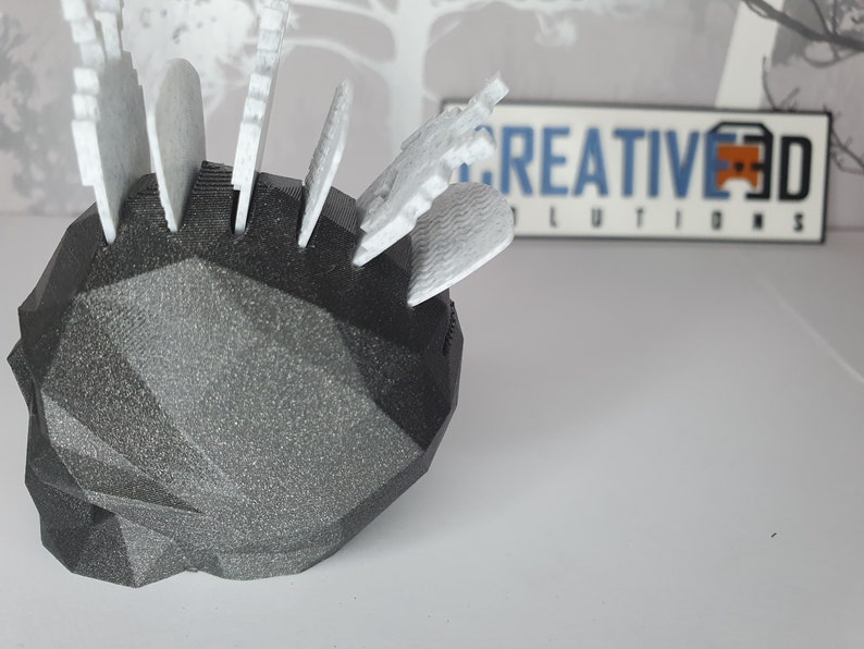 Puede incluir: Un objeto negro, geom&eacute;trico, impreso en 3D con piezas blancas, impresas en 3D, insertadas en &eacute;l. El objeto est&aacute; sobre una superficie blanca.