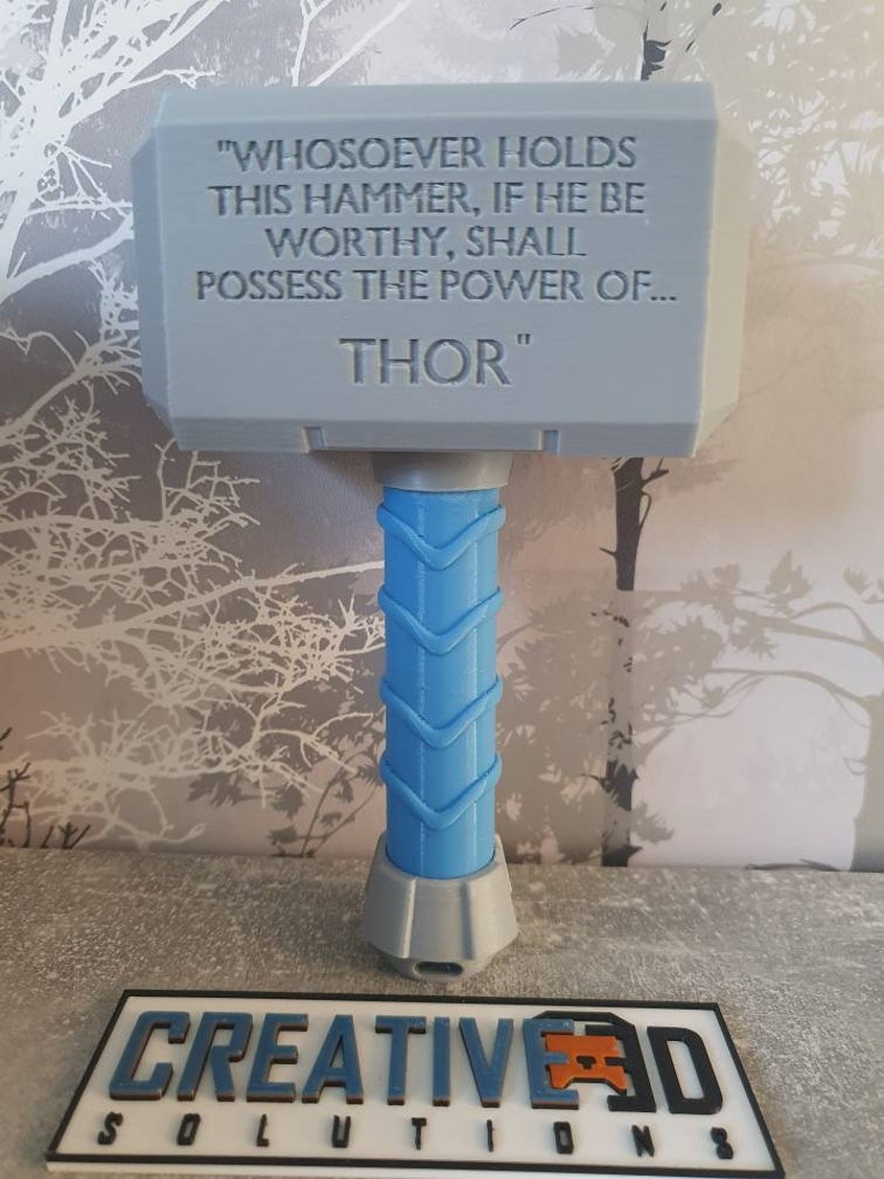 May include: A gray 3D printed replica of Thor's hammer, Mjolnir, with the inscription "WHOSOEVER HOLDS THIS HAMMER, IF HE BE WORTHY, SHALL POSSESS THE POWER OF... THOR" on the top. The hammer has a blue handle.