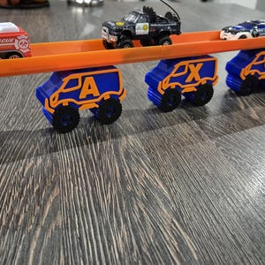 May include: A toy track set with a fire truck, two police cars, and five blue toy vans with orange letters spelling out "JAxon".