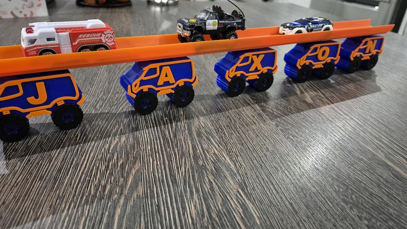 May include: A toy track set with a fire truck, two police cars, and five blue toy vans with orange letters spelling out "JAxon".