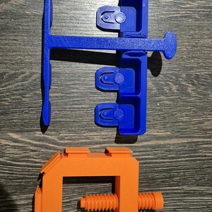 May include: A blue plastic tool with multiple slots and a handle, and an orange plastic clamp with a screw.