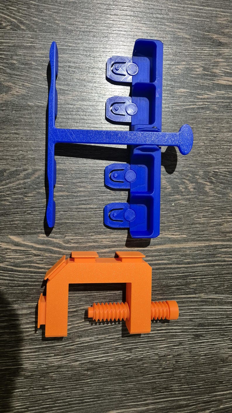May include: A blue plastic tool with multiple slots and a handle, and an orange plastic clamp with a screw.