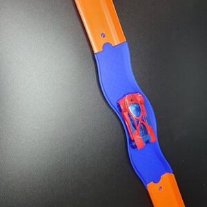 May include: A red toy car with blue accents is on a blue and orange track. The track is curved and the car is going around the curve.