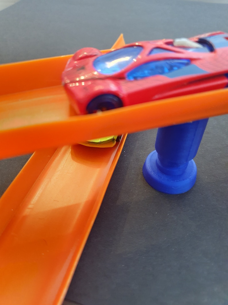 Puede incluir: Un coche de juguete rojo con ventanas tintadas azules est&aacute; en una pista de pl&aacute;stico naranja. La pista est&aacute; conectada a una base de pl&aacute;stico azul.