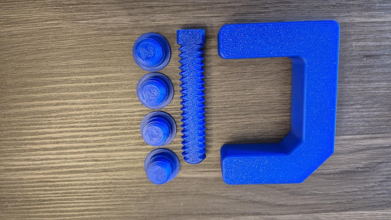May include: A blue plastic clamp with a threaded screw and four blue plastic nuts. The clamp is made of a textured plastic.