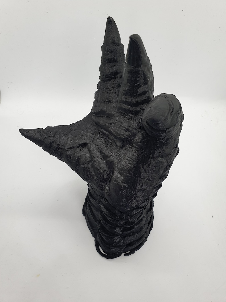 May include: A black 3D printed hand with long, sharp claws. The hand is posed in a grasping gesture, with the fingers curled inward.