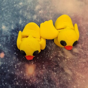 May include: Two yellow rubber duck figurines with black eyes and red beaks. The ducks are facing each other and are connected at the back.