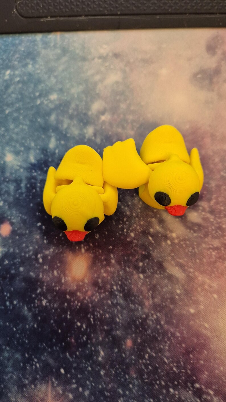 May include: Two yellow rubber duck figurines with black eyes and red beaks. The ducks are facing each other and are connected at the back.