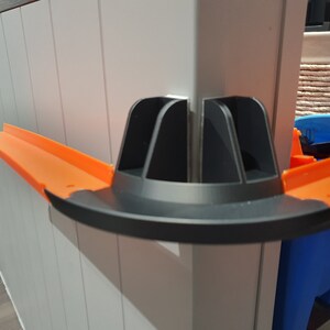 May include: A black and orange plastic track piece for a toy car racing set. The track piece is designed to connect to other track pieces and create a loop or curve in the track.