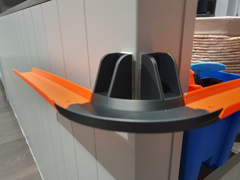 May include: A black and orange plastic track piece for a toy car racing set. The track piece is designed to connect to other track pieces and create a loop or curve in the track.