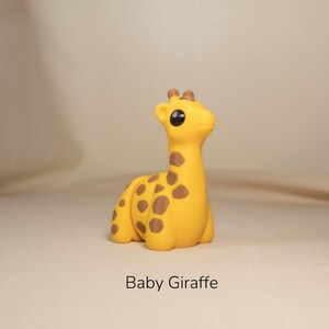 May include: A small, yellow baby giraffe toy with brown spots. The giraffe has large, black eyes and a cute expression.