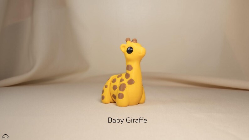 May include: A small, yellow baby giraffe toy with brown spots. The giraffe has large, black eyes and a cute expression.