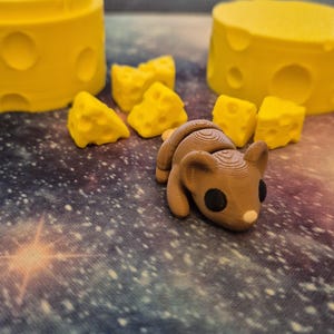 Puede incluir: Una figurita de rat&oacute;n impresa en 3D de color marr&oacute;n con ojos negros y nariz rosa, rodeada de bloques de queso amarillo.