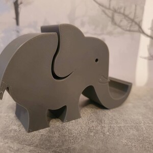 K&ouml;nnte beinhalten: Ein graues, 3D-gedrucktes Objekt in Elefantenform. Der Elefant hat einen R&uuml;ssel, Ohren und eine kleine &Ouml;ffnung auf dem R&uuml;cken. Das Objekt ist mit einer glatten, matten Oberfl&auml;che versehen und ist wahrscheinlich ein Dekorationsartikel oder ein kleiner Beh&auml;lter.