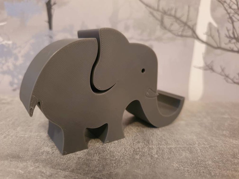 K&ouml;nnte beinhalten: Ein graues, 3D-gedrucktes Objekt in Elefantenform. Der Elefant hat einen R&uuml;ssel, Ohren und eine kleine &Ouml;ffnung auf dem R&uuml;cken. Das Objekt ist mit einer glatten, matten Oberfl&auml;che versehen und ist wahrscheinlich ein Dekorationsartikel oder ein kleiner Beh&auml;lter.