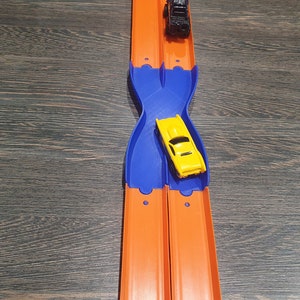 K&ouml;nnte beinhalten: Ein gelbes Spielzeugauto rast auf einer orangenen Rennbahn mit einer blauen Plastikrampe. Das Auto ist kurz davor, &uuml;ber die Rampe zu fahren und auf der Rennbahn weiterzufahren.