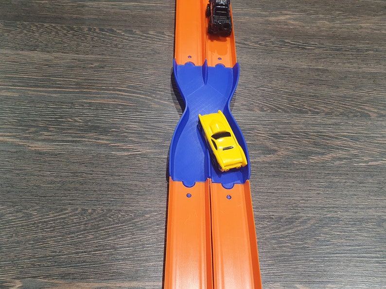 K&ouml;nnte beinhalten: Ein gelbes Spielzeugauto rast auf einer orangenen Rennbahn mit einer blauen Plastikrampe. Das Auto ist kurz davor, &uuml;ber die Rampe zu fahren und auf der Rennbahn weiterzufahren.