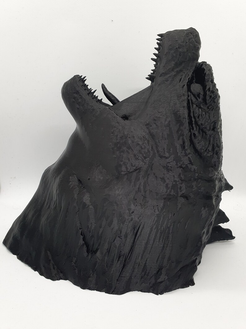 May include: A 3D printed black dragon head sculpture with an open mouth and sharp teeth. The sculpture is detailed and textured, with a rough, layered surface.