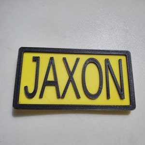 May include: A yellow name tag with a black border and the name "Jaxon" printed in black letters.