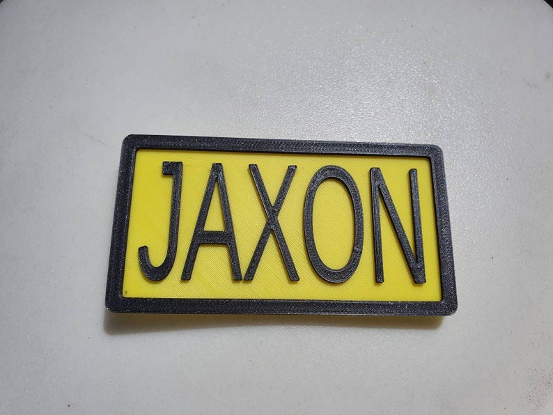 May include: A yellow name tag with a black border and the name "Jaxon" printed in black letters.