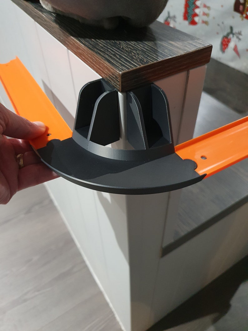 May include: Orange plastic track piece with a black plastic connector for a toy race track.